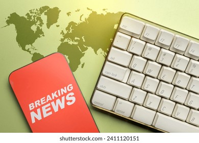 Closeup view of computer keyboard and mobile phone screen with breaking news inscription on a colored background. Live broadcasting, news, and journalism concept