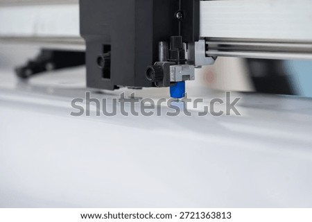 Close-up view of a computer-controlled flatbed or roller cutting machine performing precision trimming on a large sheet of vinyl wrap film. The image showcases advanced technology in the automotive aftermarket industry, highlighting automated production, digital accuracy, and the preparation stage for car wrapping or paint protection film (PPF) installation. Ideal for marketing professional wrapping services, equipment manufacturers, or illustrating modern manufacturing processes in the customization field.