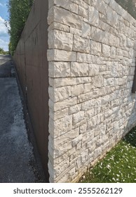 A close-up view of a corner stone wall with a textured, natural limestone finish contrasting against a smooth concrete wall on the left. 