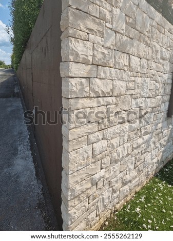 A close-up view of a corner stone wall with a textured, natural limestone finish contrasting against a smooth concrete wall on the left. 