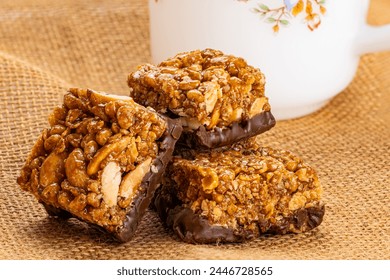 Closeup view of crispy homemade peanuts, almond and chocolate mini protein bars and white coffee cup on sack cloth. - Powered by Shutterstock