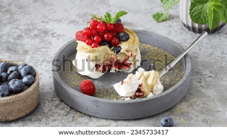 A close-up view of a cut Pavlova dessert reveals its luscious berry filling. The meringue, paired with pistachio cream, bursts with fresh raspberries, blueberries, and currants. Mint adds a refreshing
