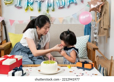 Closeup View Of Cute Asian Baby Girl Trying To Blow The Party Horn Her Mother Is Holding For Her On The Birthday Celebration At Home