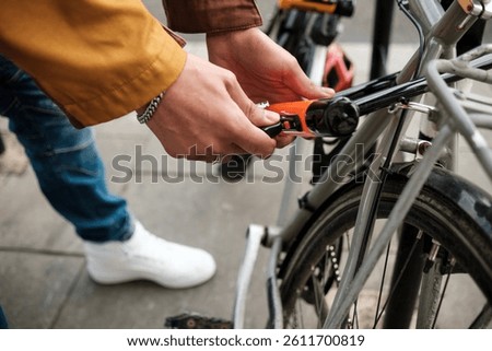 Close-up view of cyclist's hands securing a bicycle to a rack using a u-lock, providing essential protection against theft on a busy urban street filled with life