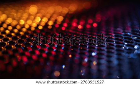 A close-up view of a dark hexagonal grid illuminated by vibrant, out-of-focus bokeh lights in shades of orange, red, and blue.