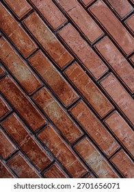 Close-up view of dark reddish-brown bricks laid diagonally, emphasizing the rough, inconsistent surface texture and dark mortar lines. Ideal as a grunge or urban background element.