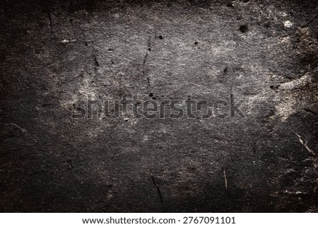 A close-up view of a dark, rough, and weathered stone wall, showcasing its grungy texture and natural imperfections.