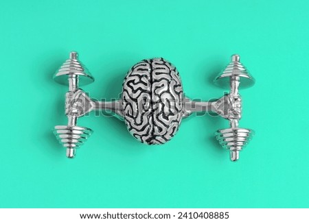 Close-up view of a detailed human brain model elevating heavy dumbbells on teal background. Creative mental strength development related concept.