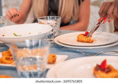 A close-up view of a dining table with plates of food, featuring a person cutting a dessert with strawberries, elegant table setting
