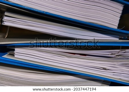 A closeup view of the documents in the blue binders piled on top of one another