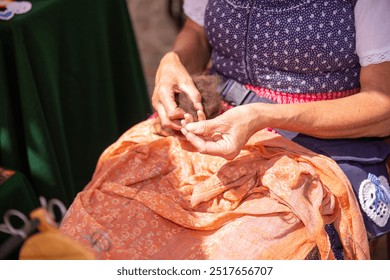 Close-up view of an elderly woman in traditional costume, spinning wool by hand during outdoor event, cultural heritage concept - Powered by Shutterstock