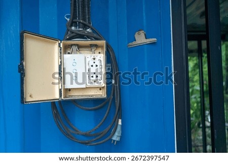 Close-up view of an electrical box mounted on a blue wall. The box is open, revealing power outlets and connected cables, showcasing utility and functionality.