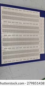 Close-up view of an electronic breadboard used for circuit prototyping, electronics experiments, engineering education, and laboratory testing. White solderless breadboard mounted on a blue educational testing board with selective focus.