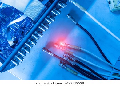 A close-up view of an electronic circuit board showcasing various colorful connections and lights. The image captures a modern technological environment.