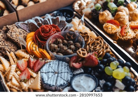 Close-up view of an elegant cheese and snack platter with assorted cheeses, olives, pretzels, grapes, strawberries, crackers, and creamy dip prepared for a luxury catering event or festive celebration.