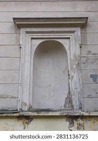 A close-up view of an empty classical architectural niche on the weathered, peeling facade of a historic mansion.