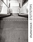 Close-up view of an empty escalator going down, captured from the top step with a focus on the metallic grooves and glass side panels. Indoor, copy space