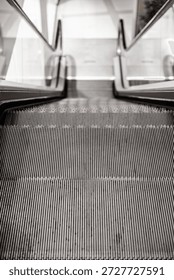 Close-up view of an empty escalator going down, captured from the top step with a focus on the metallic grooves and glass side panels. Indoor, copy space