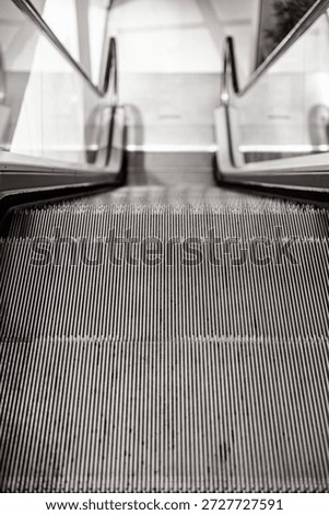 Close-up view of an empty escalator going down, captured from the top step with a focus on the metallic grooves and glass side panels. Indoor, copy space