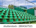 Close-up view of empty green spectator seats at an outdoor tennis stadium under a blue sky. The image highlights modern sports infrastructure designed for tournaments, competitions, training sessions and public events. Suitable for concepts related to stadium architecture, spectator seating, recreation, athletics, sports facilities, outdoor venues, championships, sporting events and active lifestyles.