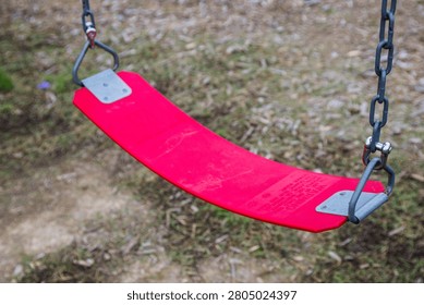 A close-up view of an empty red rubber swing seat hanging from metal chains at a playground, waiting for someone to use it for recreation.