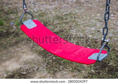 A close-up view of an empty red rubber swing seat hanging from metal chains at a playground, waiting for someone to use it for recreation.