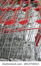 A close-up view of empty wire shopping trolleys with red handles neatly nested and arranged in rows inside a local retail grocery store or market.