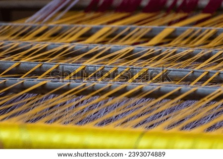 A close-up view of the essential materials of the textile industry: yarn, dye, and wood. The yarn, made from a variety of fibers, is the foundation of all textile products. The dye, a rainbow of color