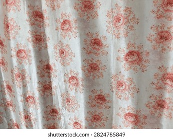 A close-up view of a fabric with a repeating pattern of soft pink roses and green leaves, creating a vintage and romantic aesthetic.