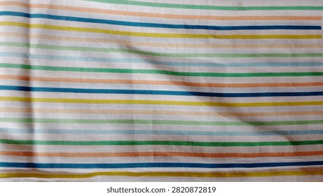 A close-up view of a fabric surface featuring a repeating pattern of horizontal stripes in soft pastel colors including green, blue, orange, and yellow.