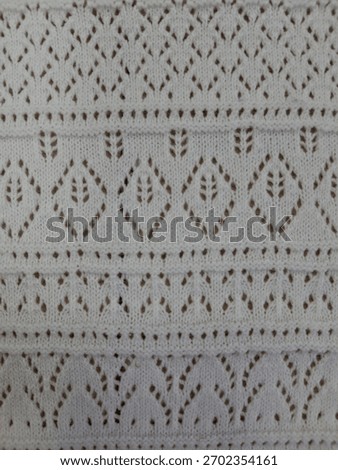 A close-up view of a fabric or surface featuring a repeating geometric pattern composed of small dark dots arranged in diamond and arc shapes