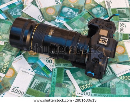 Close-up view features a professional camera and telephoto lens on a bed of Kyrgyzstani som banknotes. The arrangement highlights themes of photography and finance.