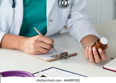 Close-up view of female doctor hand holding bottle with pills and writing prescription. Healthcare, medical and pharmacy concept.