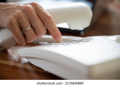 Closeup view of female hand dialing telephone number using white landline phone. - Shutterstock ID 2176830889