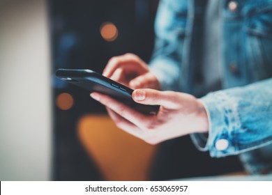 Closeup View Of Female Hands Holding Modern Smart Phone And Pointing Fingers On The Touch Screen At Night.Horizontal, Blurred Background, Bokeh Effects