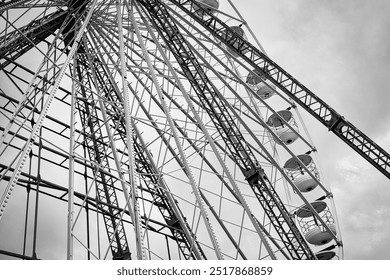 A close-up view of a ferris wheel structure, showcasing its intricate metal framework and gondolas against a cloudy sky, in black and white.In Blackpool, UK. - Powered by Shutterstock