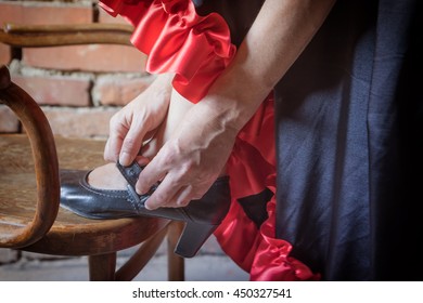 Closeup View Of A Flamenco Dancer With Her Foot On An Old Wooden Chair And Putting On The Black Old Shoe. The Photo Has Deliberately Darkened Edges