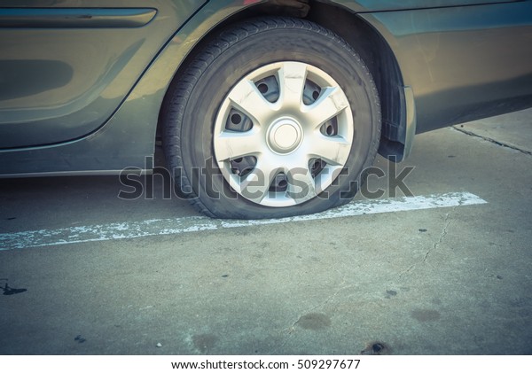 Close-up view flat rear tire on a car. Detail of\
car wheel flat tire on the road, parking lot. Burst tire\
background. Motor Vehicle Insurance and roadside assistance\
concept. Vintage filter\
look.