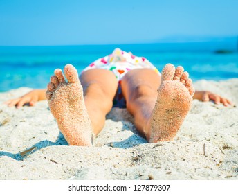 Close-up view of foots by the girl lying on the sand beach.