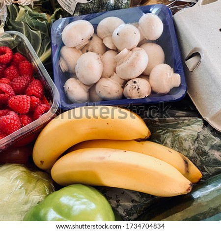 Closeup view of fresh fruit & vegetables filling the frame with healthy color. Raspberries, bananas, mushrooms & salad greens in a crate of mixed fruit and veg. Organic & nutritional food background.
