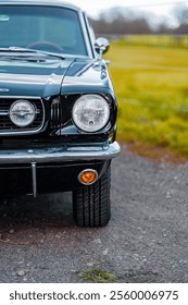 A close-up view of the front section of a classic black car showcasing its shiny chrome headlights, elegant vintage detailing, and unique character on a rustic outdoor backdrop.
