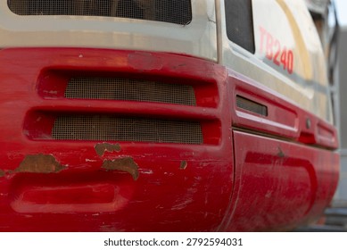 Close-up view of the front side of a weathered red and white locomotive showing metal vents, grilles, worn paint, scratches, and industrial surface detail