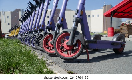 Close-up view of front wheels of dockless e-scooters at a rental station under bright summer sun, illustrating sharing-economy transport. Photo. Selective focusing