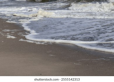 Close-up view of gentle ocean waves reaching the sandy beach, leaving a foamy trail as the water recedes back into the sea. - Powered by Shutterstock