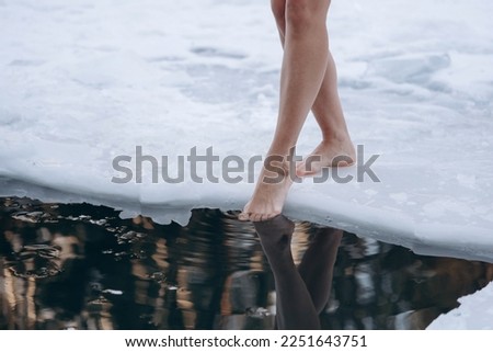 close-up view of girl legs standing on snow near ice hole getting into cold water in winter, healthy lifestyle, tempering concept