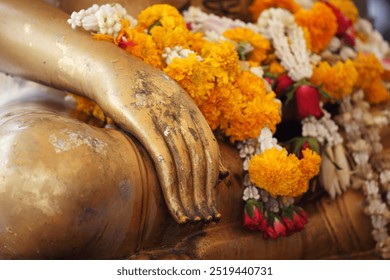 A close-up view of a golden Buddha statue's hand adorned with vibrant flowers, symbolizing devotion and spirituality in a serene setting. - Powered by Shutterstock