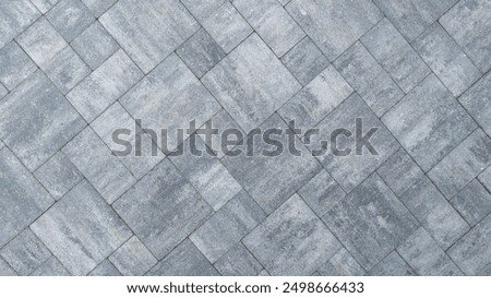A close-up view of a gray paved surface arranged in a herringbone pattern, showcasing its textured design and color variations.
