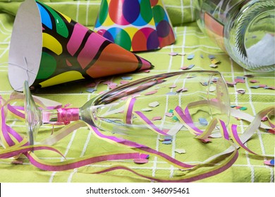 Closeup View Of A Green Tablecloth After A Party Celebration With Confetti, Empty Bottle And Party Popper. Champagne Glass With Lipstick Imprint Is Lying In The Foreground. 