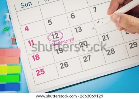Close-up view of hand using pen to draw pink circle on calendar with write word Anniversary and heart. Concept of wedding anniversaries, company anniversary, and celebrations.