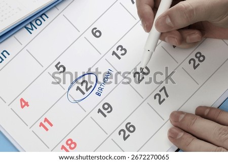 Close-up view of hand using pen to draw blue circle on calendar with write word Birthday. Concept of anniversaries, celebrating birthdays, party planning and gift surprises.